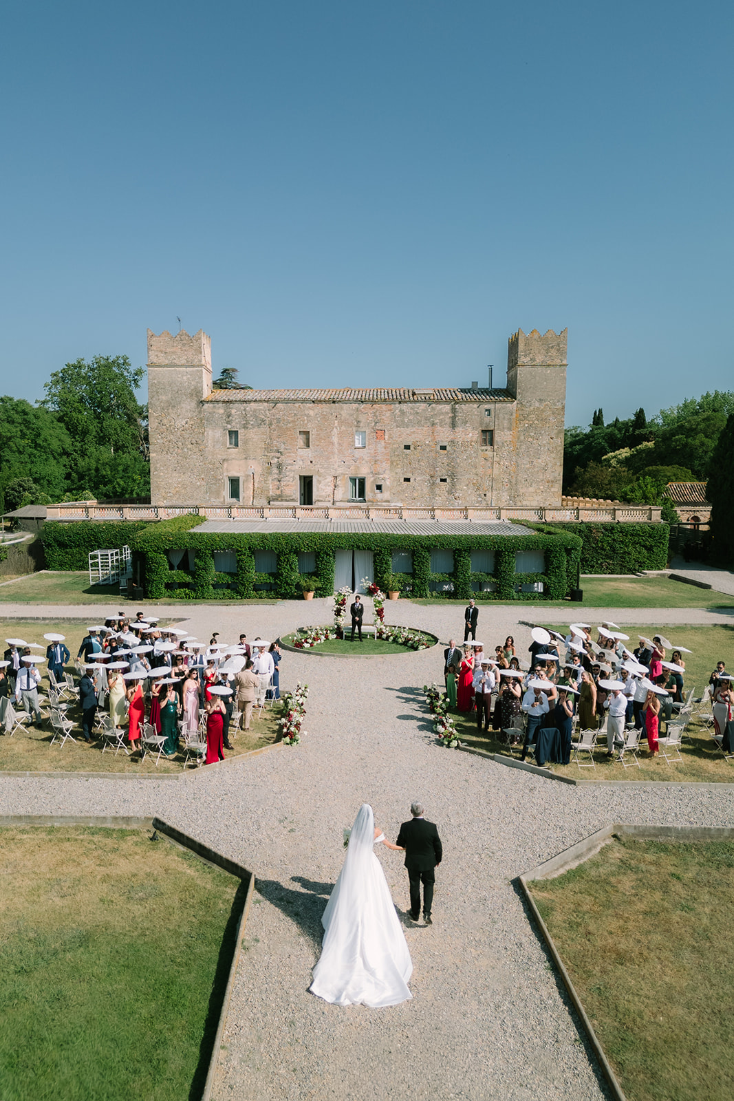 Novia entrando a la ceremonia junto a un castillo medieval con invitados a ambos lados