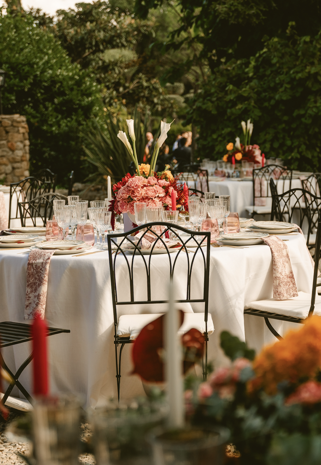 Mesa de banquete con mantelería blanca, servilletas estampadas y centro floral rojo y rosa